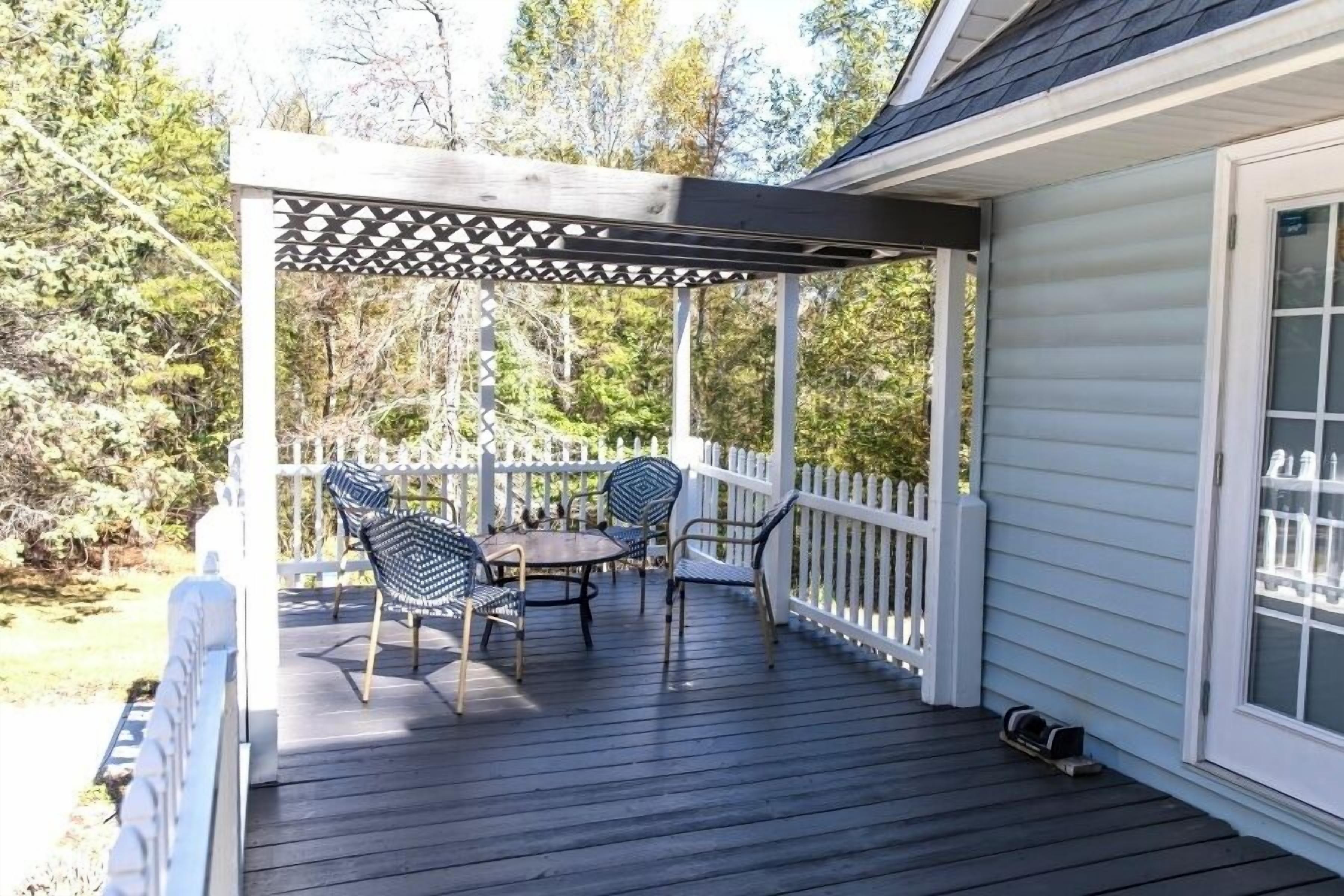 A covered outdoor deck with a pergola, a table, and four chairs.