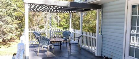 A covered outdoor deck with a pergola, a table, and four chairs.