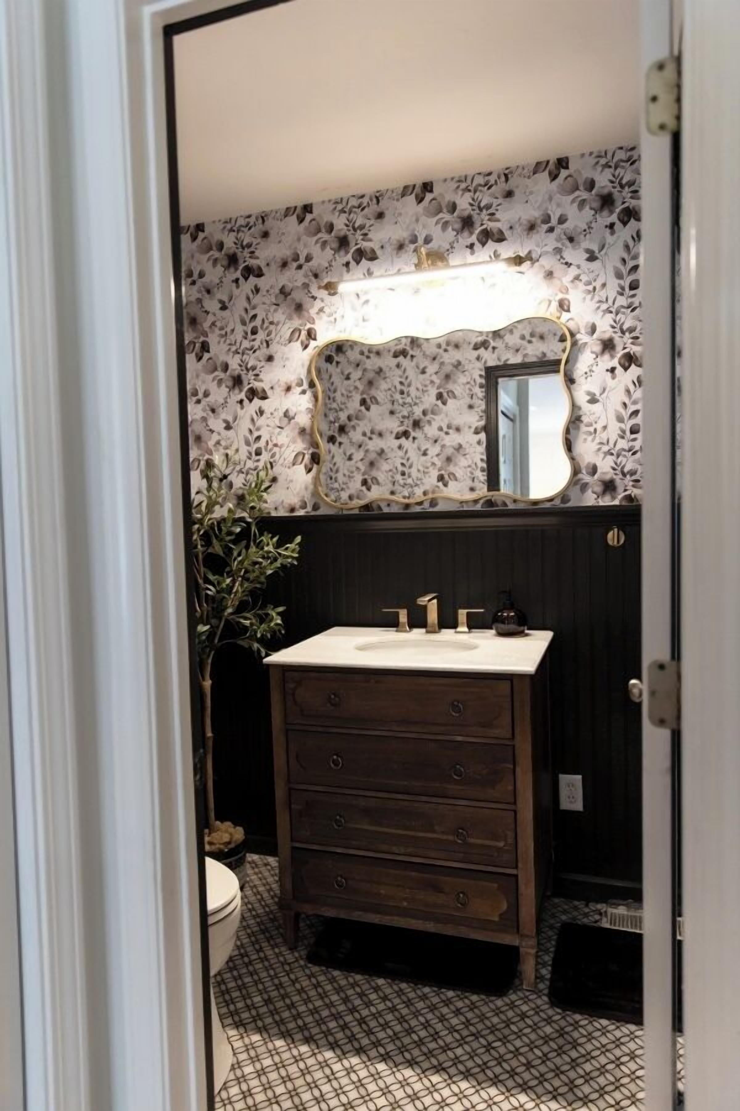 A bathroom with a floral wallpaper, a wooden vanity, a sink, and a mirror.