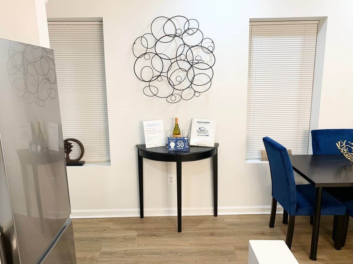 A modern kitchen with a refrigerator, a dining table with chairs, and a wall-mounted abstract art piece.