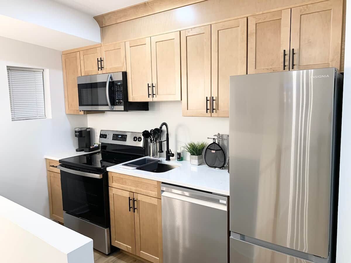 A modern kitchen with stainless steel appliances, wooden cabinets, and a white countertop.