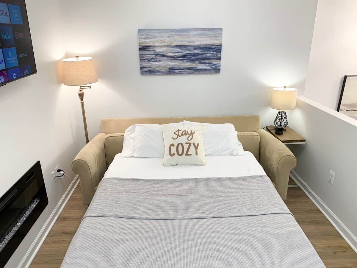 A neatly arranged bedroom with a bed, two bedside lamps, a wall-mounted TV, and a painting above the bed.