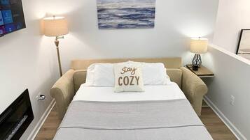 A neatly arranged bedroom with a bed, two bedside lamps, a wall-mounted TV, and a painting above the bed.