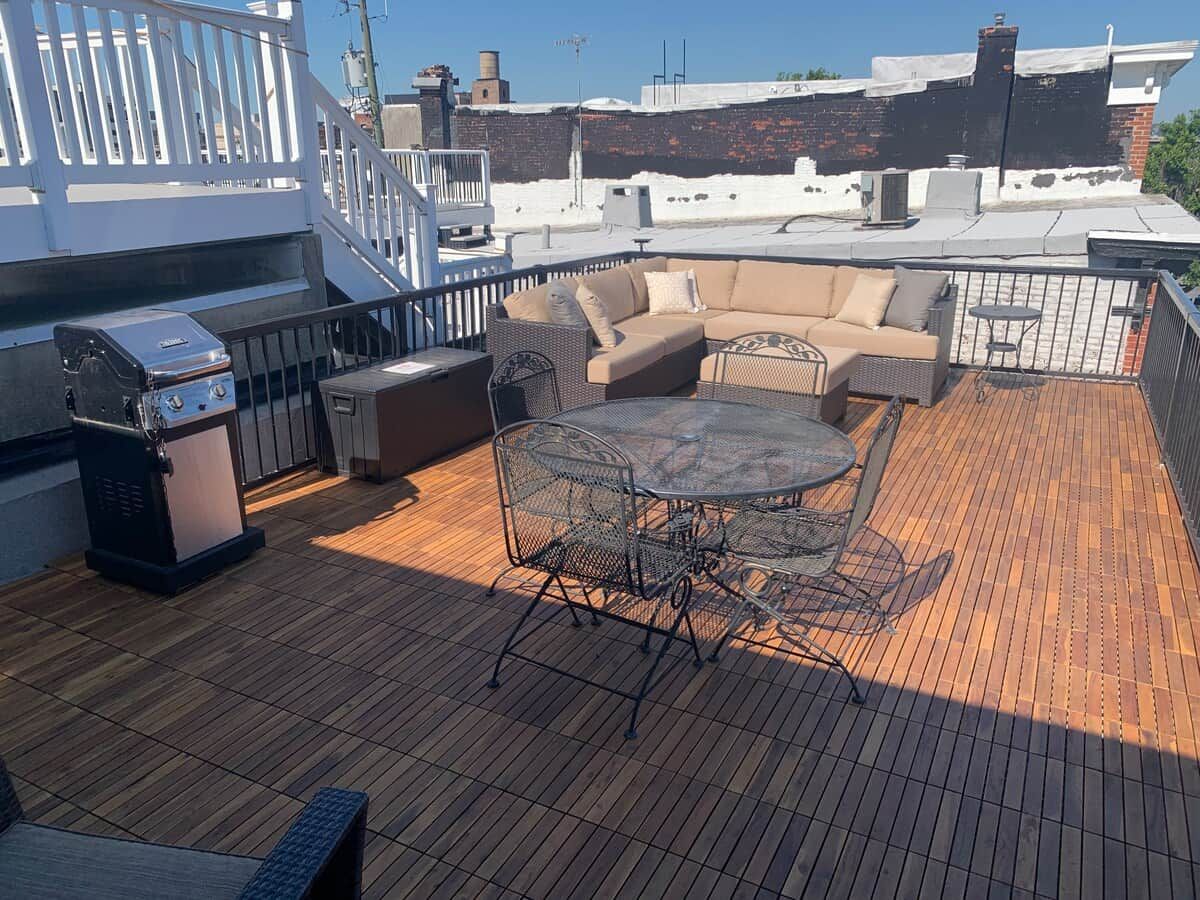 A rooftop deck with a grill, round table, chairs, and a sofa.