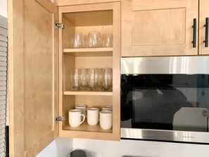 A kitchen with wooden cabinets, a stainless steel oven, and shelves with glassware and mugs. - Lavish Luxe 2BD/1BA apartment in Federal Hill (Baltimore)
