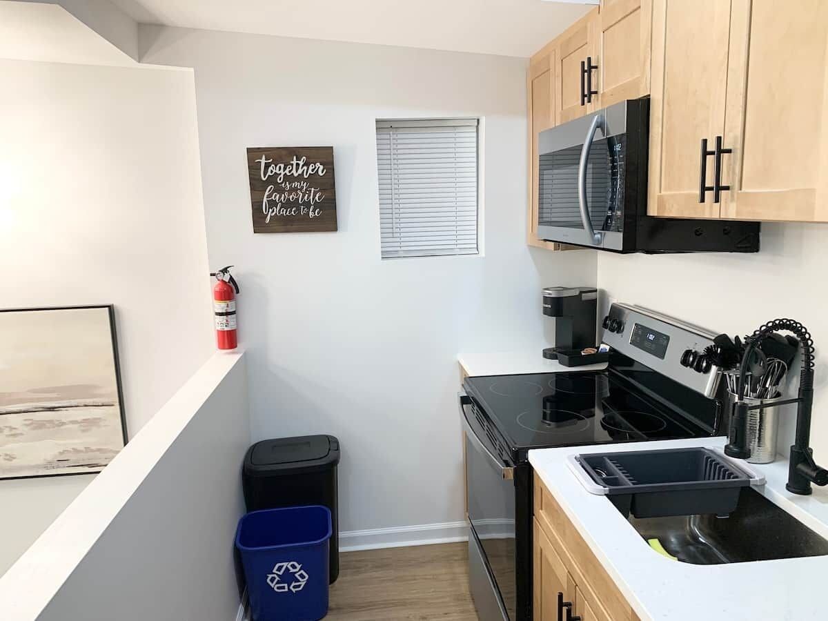 Cocina compacta con estufa, microondas y lavaplatos. Hay un extintor y un cubo de basura.