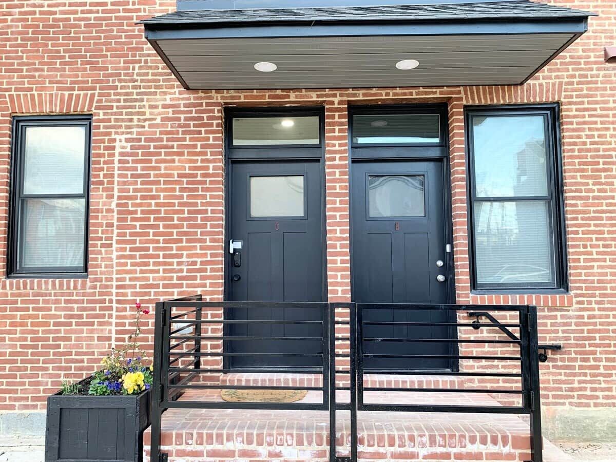 A brick building with two black doors and a small porch with a black railing.