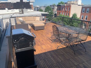 Una terraza en la azotea con una parrilla, muebles de exterior y una mesa con sillas.