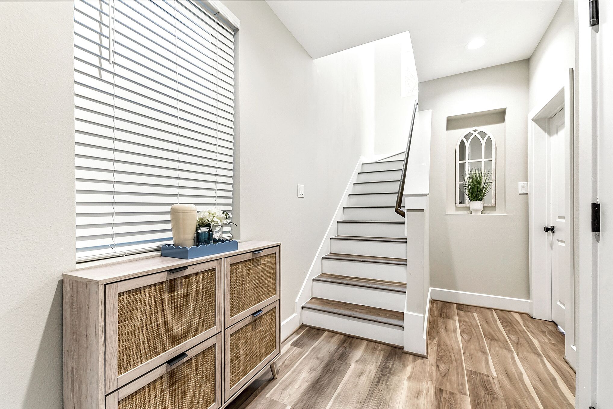 A staircase leading to a landing with a white door and a window with blinds.
