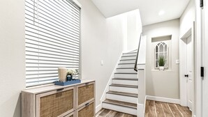 Una escalera que sube a un rellano con una puerta blanca y una ventana con persianas.