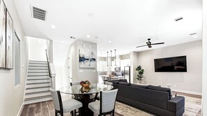 Una sala de estar moderna con una mesa de comedor de cristal, sofás grises y un televisor de pantalla plana montado en la pared.