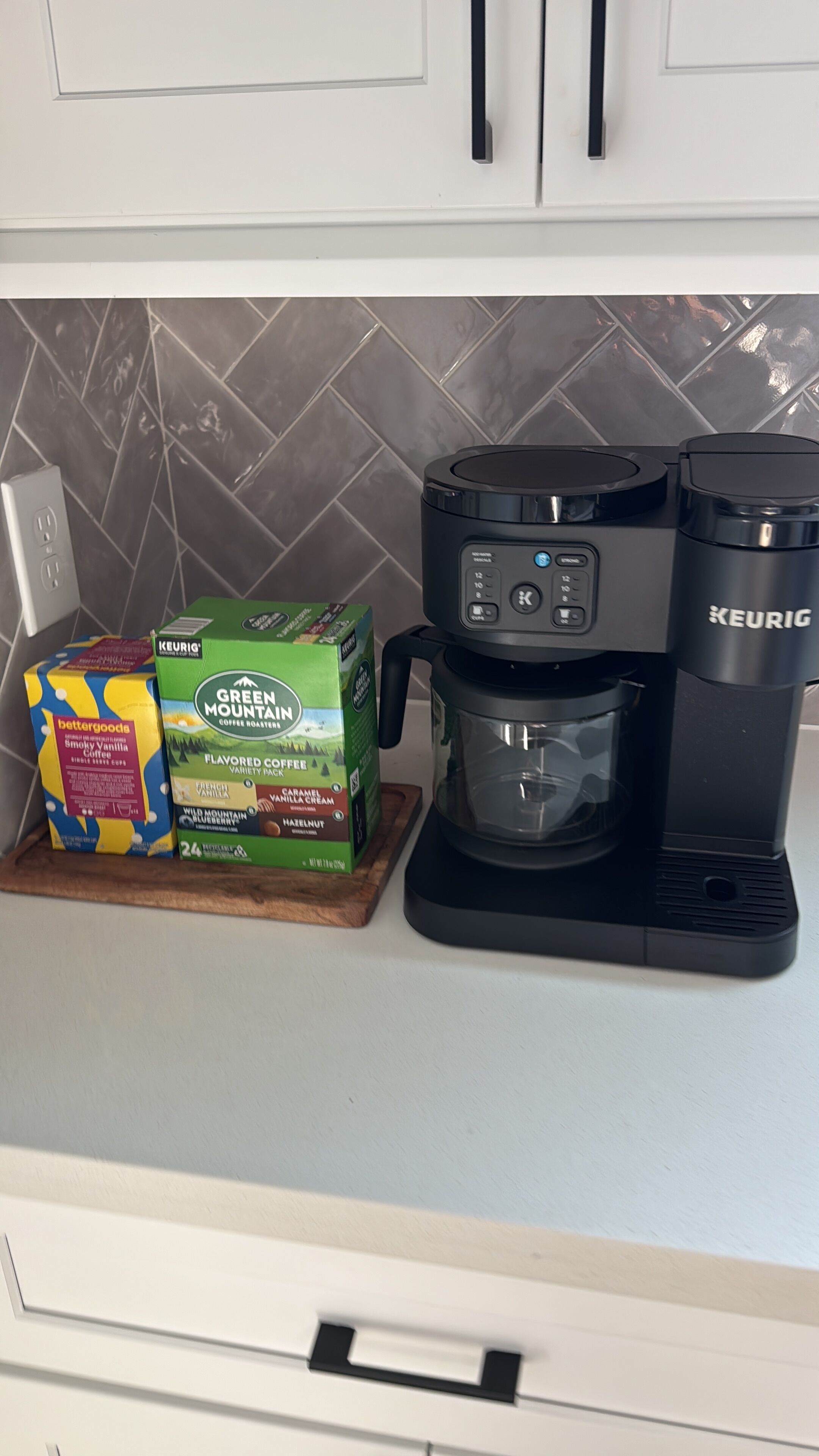 A kitchen counter with a coffee maker, a box of coffee pods, and a box of coffee creamers.