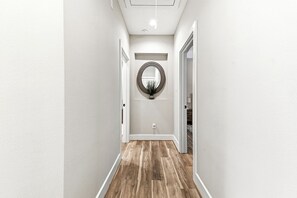 A hallway with a wooden floor, a round mirror on the wall, and a ceiling light. - Upscale Gated 3BR wGarage Near CityCentre & Memorial (Houston)
