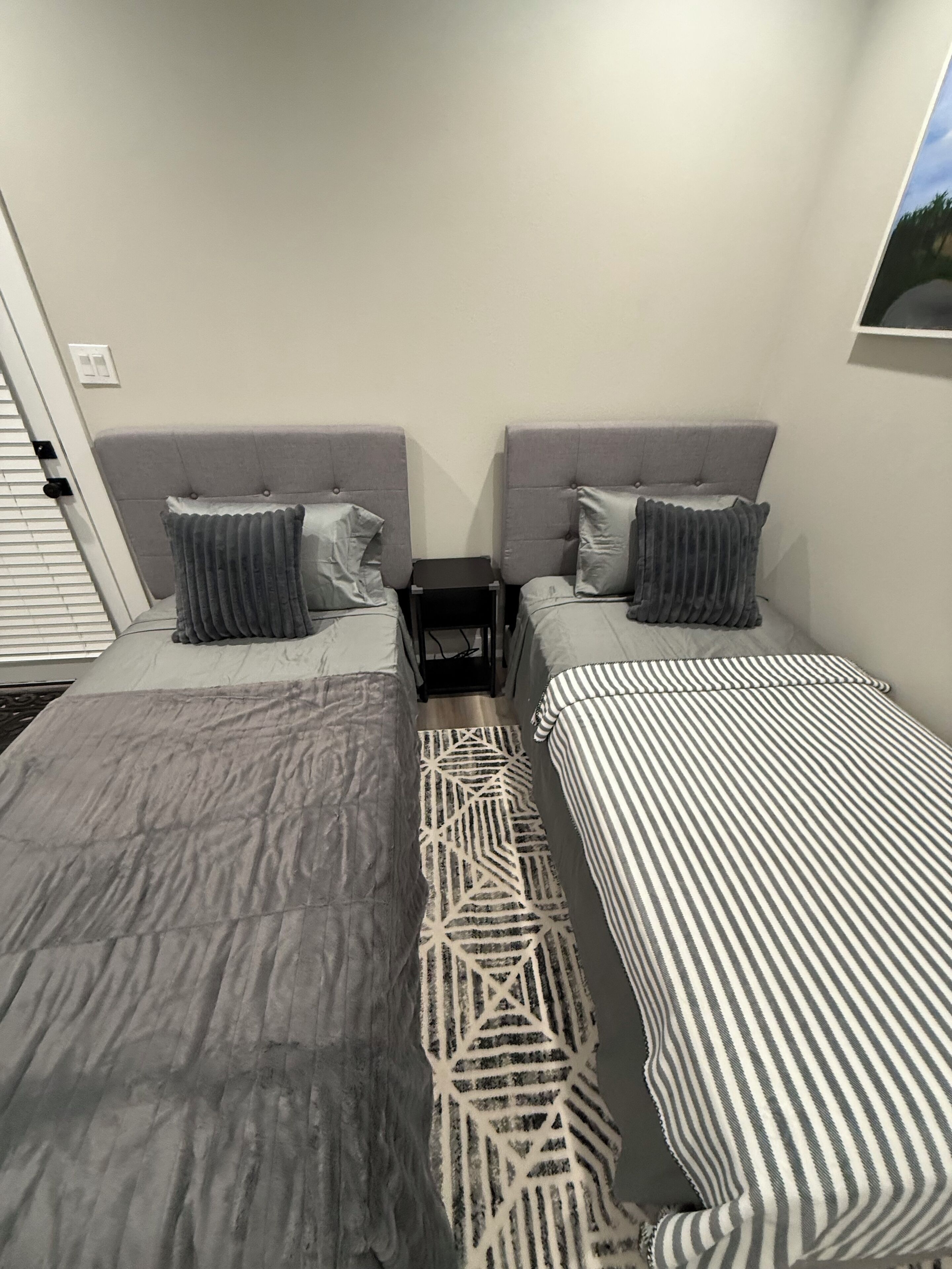 A room with two beds, each with a headboard, a small bedside table, and a pillow.