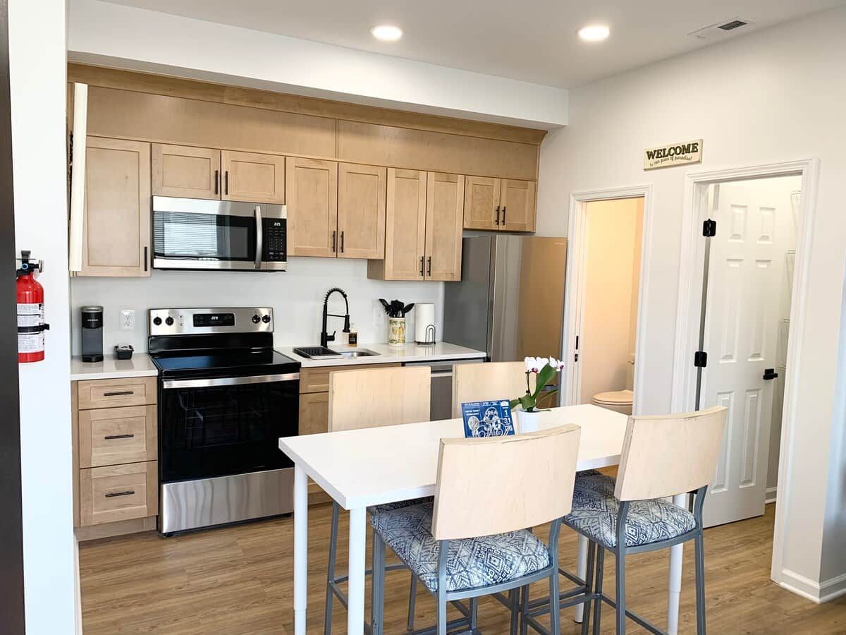A modern kitchen with stainless steel appliances, wooden cabinets, and a dining area with two chairs and a table.