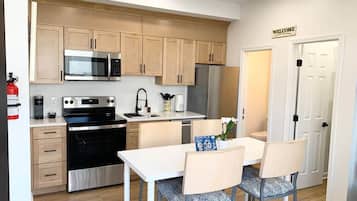 A modern kitchen with stainless steel appliances, wooden cabinets, and a dining area with two chairs and a table.
