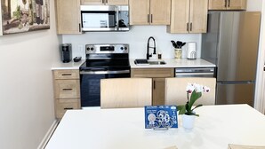 A modern kitchen with wooden cabinets, stainless steel appliances, and a dining table with a potted orchid.
