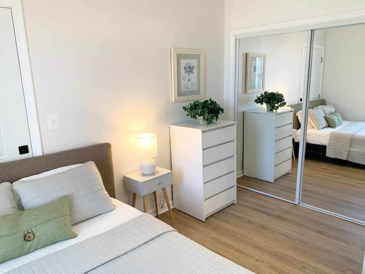 A bedroom with a bed, bedside table, dresser, and a mirror.