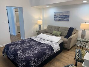 A bedroom with a bed, a sofa, a glass table, and a painting on the wall. - Comfy Cozy 2BD/1.5BA apt in Federal Hill (Baltimore)