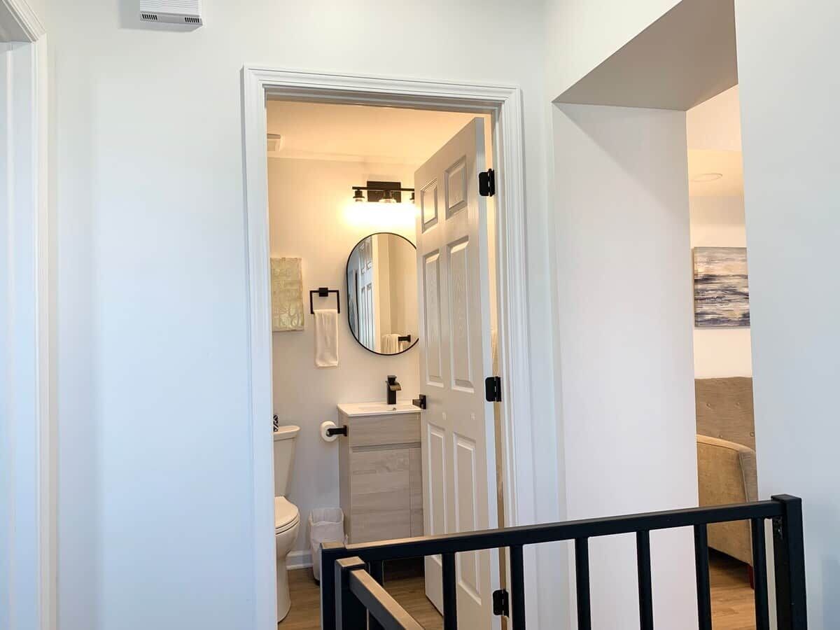 Un couloir menant à une salle de bain équipée de toilettes, d’un lavabo et d’un miroir.