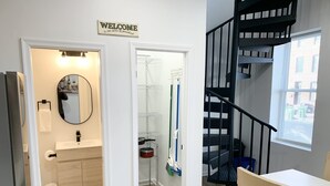 A modern bathroom with a sink, mirror, and toilet. There is a welcome sign above the door, and a staircase with a black railing leads to another level.