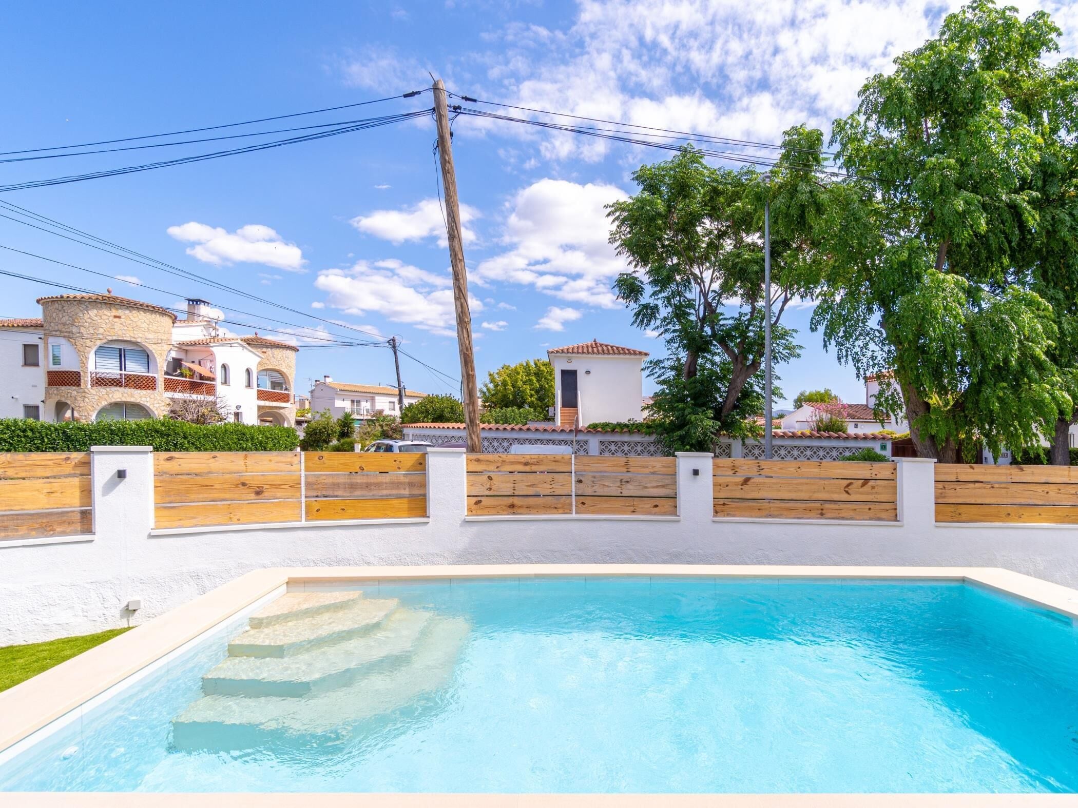 Piscina com cerca de madeira, muro de pedra e vista para casas ao fundo.