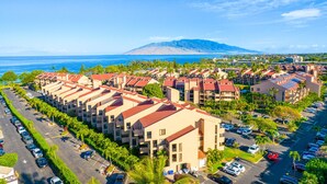 A resort with multiple buildings, a parking lot, and a mountain in the background. - Beach, Pool & Pickleball Short Walk to Beach! (Kihei)