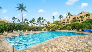 A swimming pool with stone tiles, surrounded by palm trees and lounge chairs. - Beach, Pool & Pickleball Short Walk to Beach! (Kihei)