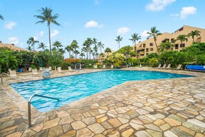 A swimming pool with stone tiles, surrounded by palm trees and lounge chairs. - Beach, Pool & Pickleball | Maui Kihei Condo (Kihei)