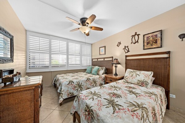 A bedroom with two beds, a ceiling fan, a nightstand with a lamp, a dresser, and a window with blinds. - Beach, Pool & Pickleball Short Walk to Beach! (Kihei)