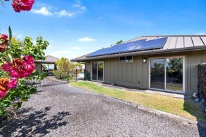 A modern building with solar panels, a gravel driveway, and a garden with pink flowers. - 🏖️Private Luxury Home at Waikoloa Beach Resort | Pool, Outdoor TV, Sleeps 8 (Waikoloa)
