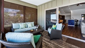 Un espacio exterior cubierto con mobiliario de mimbre, una mesa de comedor y vistas hacia el interior de la casa.