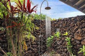 Ein Wasserfall mit einer Metallstruktur, umgeben von tropischen Pflanzen und einer Felswand.