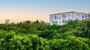 A white multi-story building with balconies, surrounded by dense green foliage. - 1 bedroom gorgeous apartment in Orosei (Orosei)