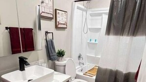 Une salle de bain moderne avec un lavabo, des toilettes et une zone de douche, le tout de couleur blanche.