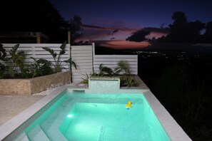 Una piscina con una cascada, rodeada por un muro blanco y plantas.