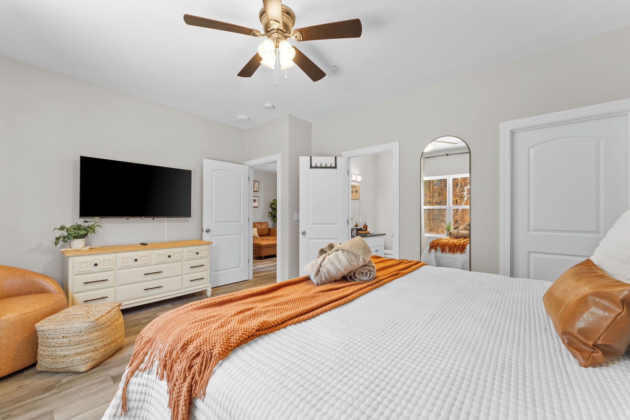 A bedroom with a bed, a TV, a ceiling fan, a dresser, and a mirror.