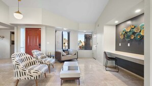 Ein modernes Wohnzimmer mit einer Couch, Sesseln und einem Couchtisch. Es gibt eine Essecke mit einer Bank und einem an der Wand befestigten dekorativen Gegenstand.