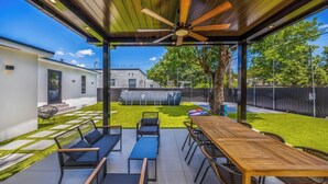 An outdoor patio with a wooden table and chairs, a ceiling fan, and a view of the backyard. - New Design Dist Escape:Pool| HotTub|Basketball Ct (Miami)