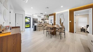 A modern kitchen with a central island, a dining area with a round table and chairs, and a bedroom with a bed and nightstand. - New Design Dist Escape:Pool| HotTub|Basketball Ct (Miami)