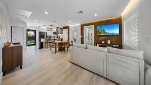 A modern living room with a large TV, a sofa, and a dining area with a table and chairs. - New Design Dist Escape:Pool| HotTub|Basketball Ct (Miami)