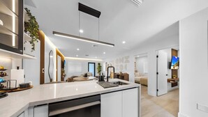 A modern kitchen with a central island, built-in appliances, and a dining area with a sofa and table. - New Design Dist Escape:Pool| HotTub|Basketball Ct (Miami)