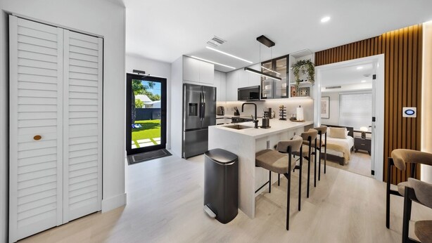 A modern kitchen with a central island, bar stools, and a view of a backyard. - New Design Dist Escape:Pool| HotTub|Basketball Ct (Miami)
