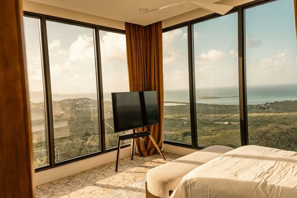 Ein Hotelzimmer mit großem Fenster, einem Bett, einem Flachbildfernseher auf einem Holzständer und einem Boden mit Steinmuster.