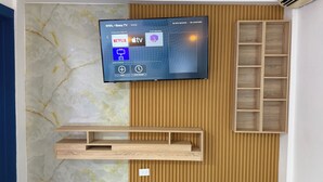 A flat-screen TV mounted on a wall with a wooden panel design, a wooden shelf below, and a marble-like wall texture. - Urban Oasis Room - Exclusive Comfort No. 5 (Playa Juan Dolio)