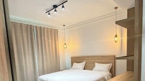 A modern hotel room with a large bed, a wooden nightstand, a chair, and a ceiling light fixture. - Urban Oasis Room - Exclusive Comfort No. 5 (Playa Juan Dolio)
