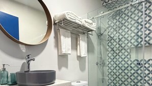 A modern bathroom with a round mirror, a sink with a wooden vanity, a toilet, and a glass shower enclosure. - Urban Oasis Room - Exclusive Comfort No. 5 (Playa Juan Dolio)