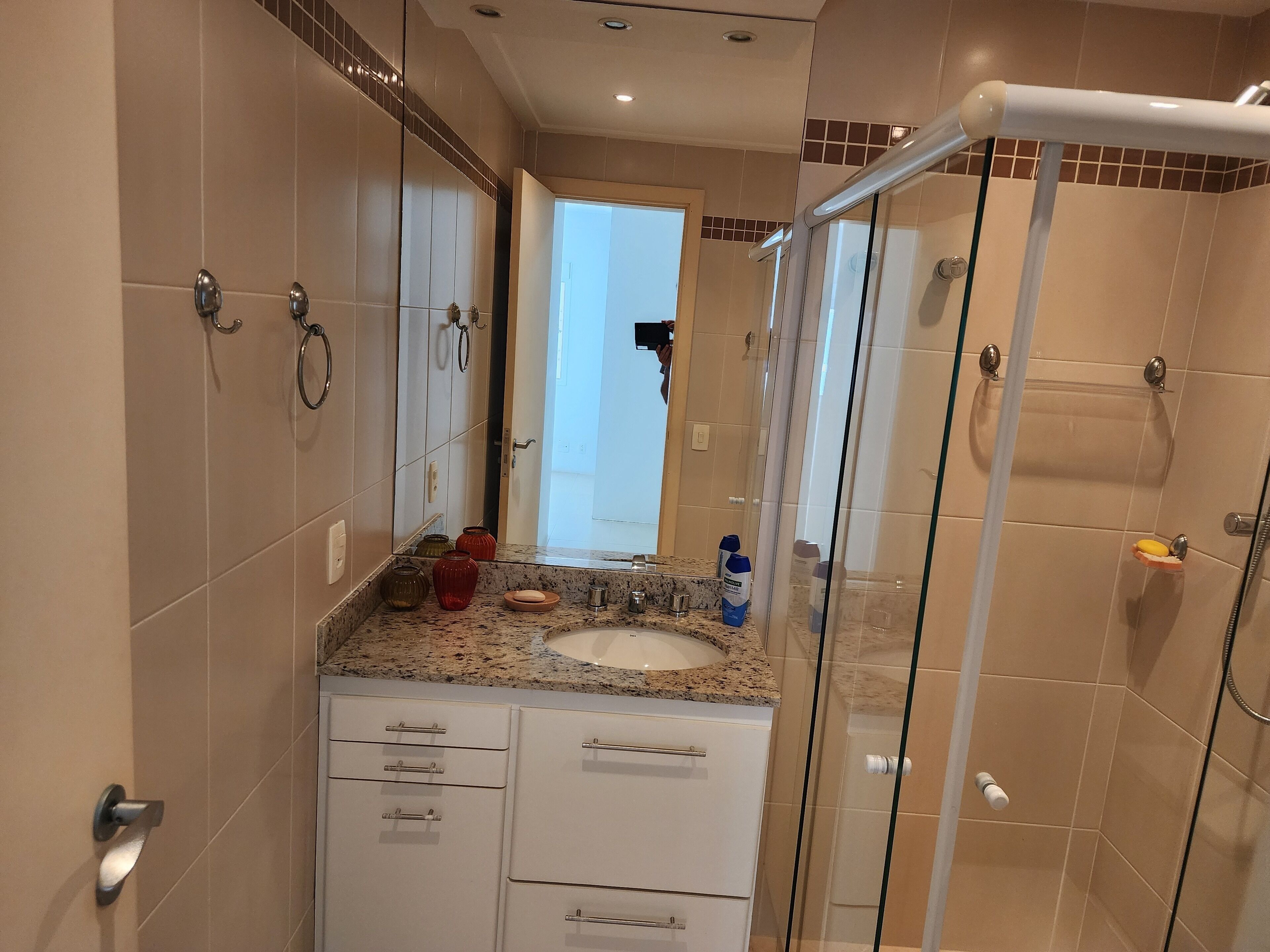 A modern bathroom with a glass shower enclosure, a sink with a granite countertop, and a mirror above the sink.