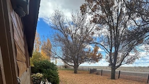 A wooden building with a porch, a vintage wagon wheel, and a flower bed with yellow and red flowers. - Amazing Country Farm in charming Del Norte perfect for large groups and families (Del Norte)