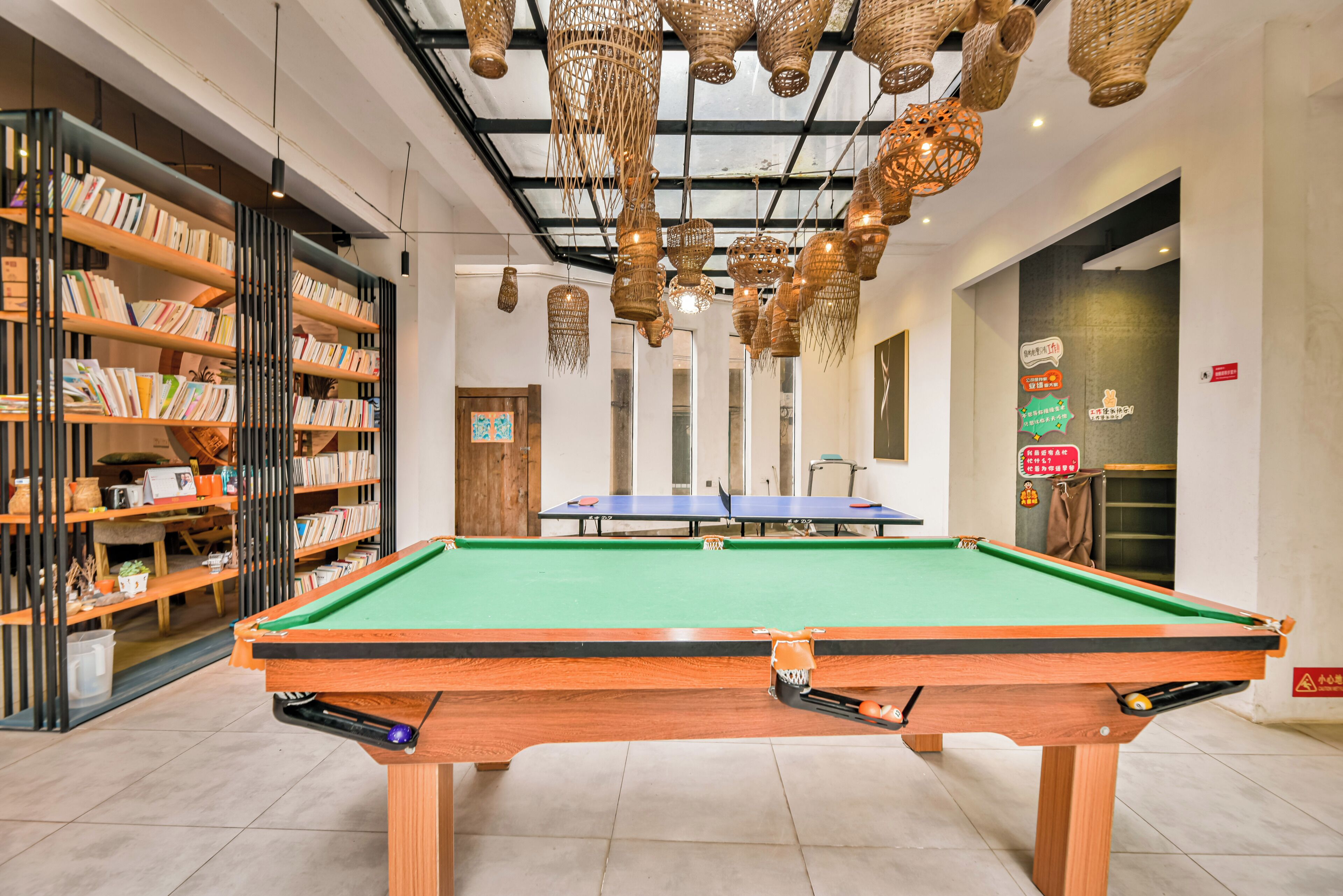 A billiards table with a green felt surface, surrounded by bookshelves and hanging wicker baskets.